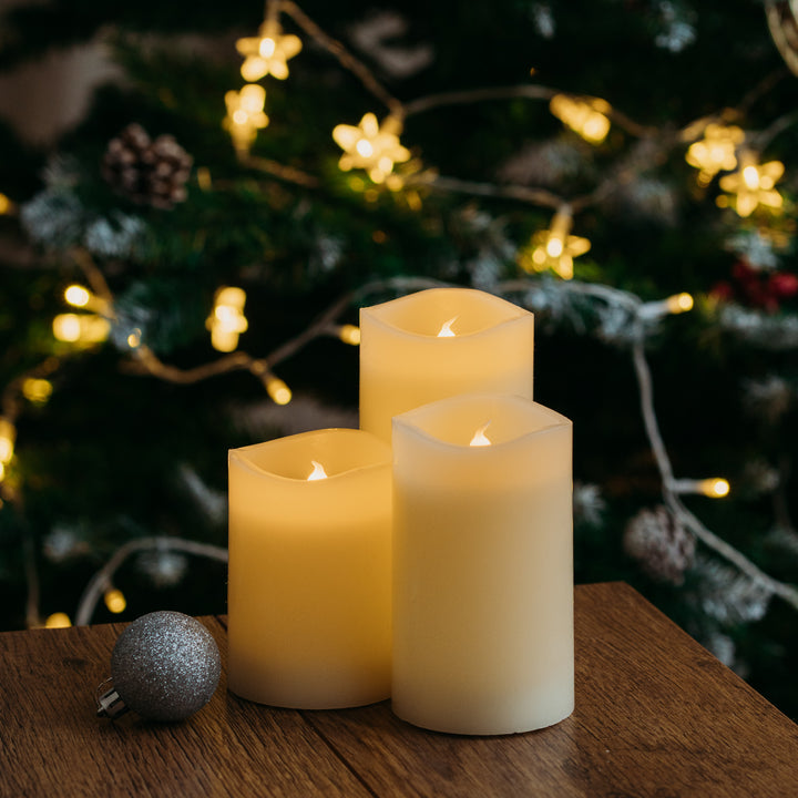 Three candles from the LED set placed on a table, Christmas tree in the background