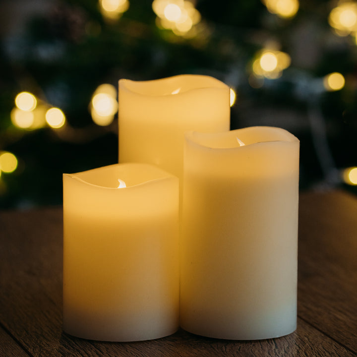Three LED candles from the set glowing on a table with a Christmas tree in the background